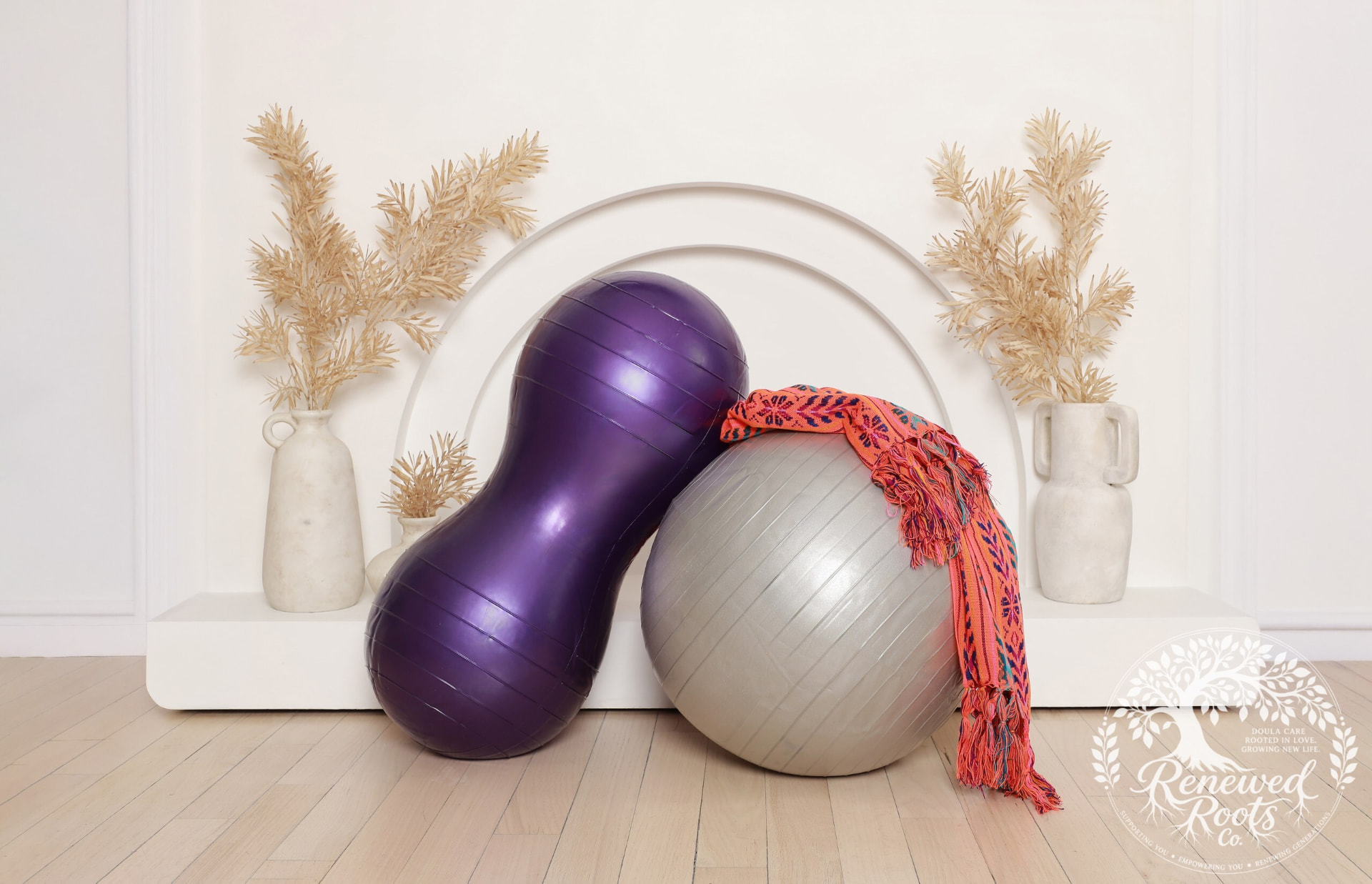 A purple peanut birth ball and silver birthing ball styled with a woven rebozo scarf and dried botanicals